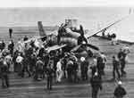 Flight deck crews gather around a VT(N)-90 Avenger whose gear collapsed during landing.