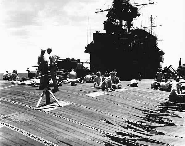 Men relax on Enterprise CV-6's buckled flight deck, as she returns to Pearl Harbor, May 1945.