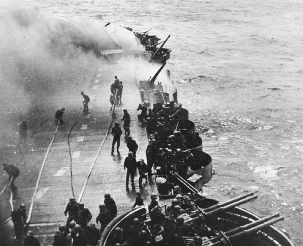 Damage control teams prepare to fight a flight deck fire caused by a near miss, 11 April 1945.