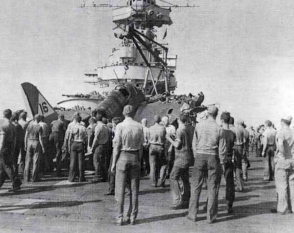 Plane handlers gather around a Bombing Twenty SB2C Helldiver that has crashed on the flight deck.